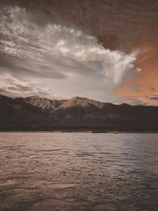 a cloudy sky above mountains and water