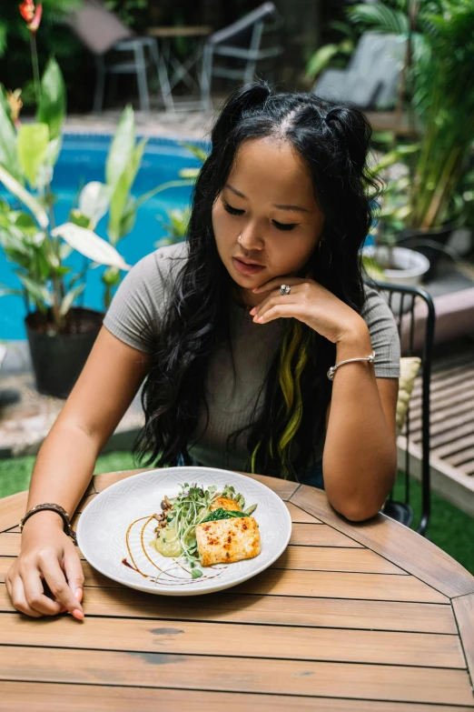 a beautiful young woman sitting at a table in front of a plate of food