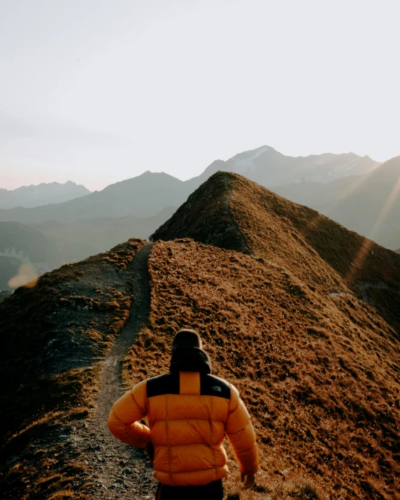 a man in a yellow puffy coat stands at the top of a hill