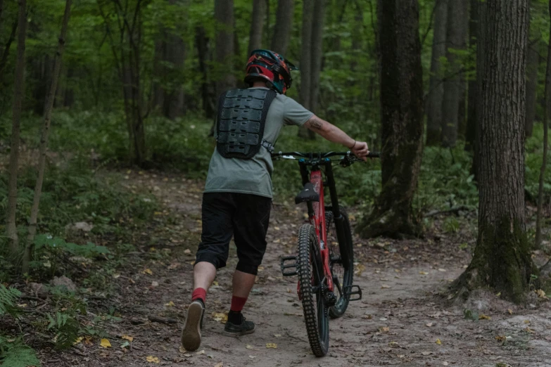 a man in a helmet is walking his bike through the woods