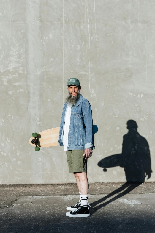 the old man stands in front of a grey wall and skateboards