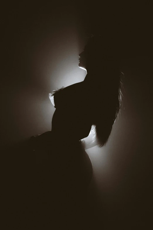 a woman in silhouette on dark, dim background with light