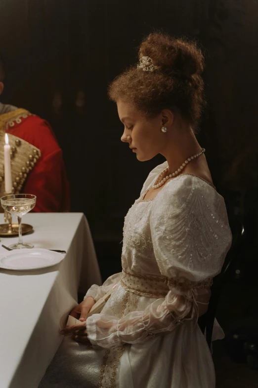 a woman is sitting in a white gown next to a candle