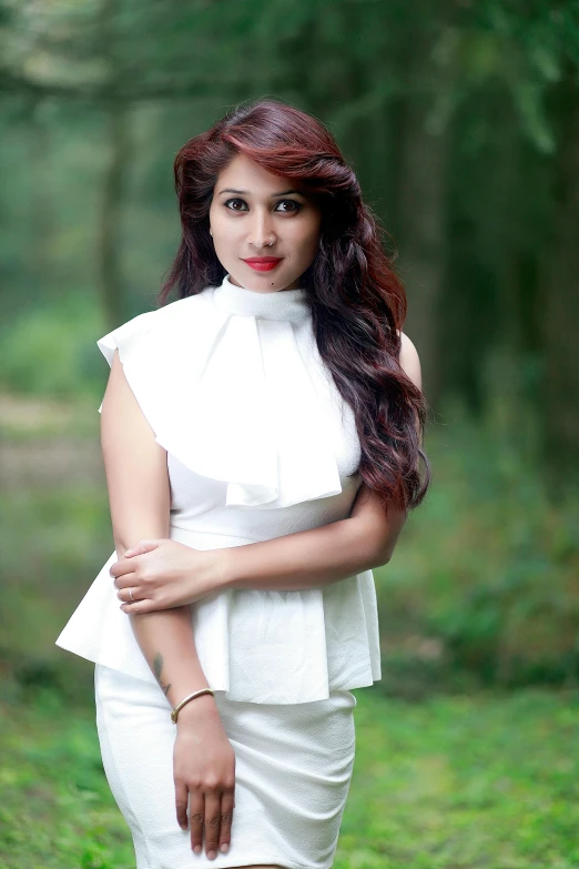 a woman posing in a white dress with a forest in the background