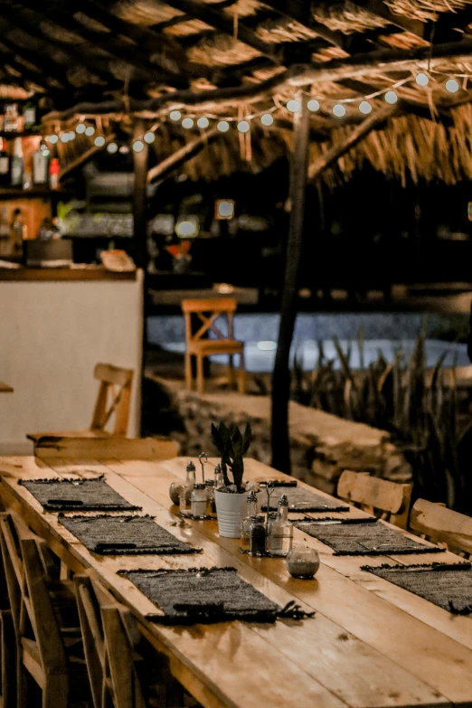 a long table set for a meal under a straw hut