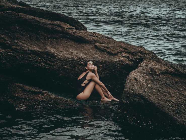 a woman sits on the rocks in the water