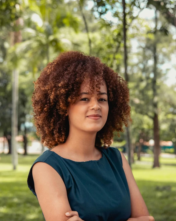 a woman with an afro standing with her arms folded and looking at the camera