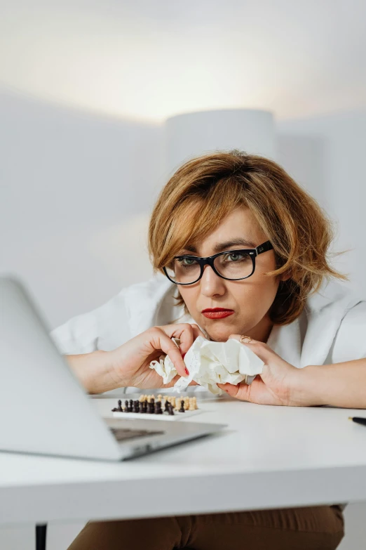 a woman in glasses leaning down as she looks at a laptop