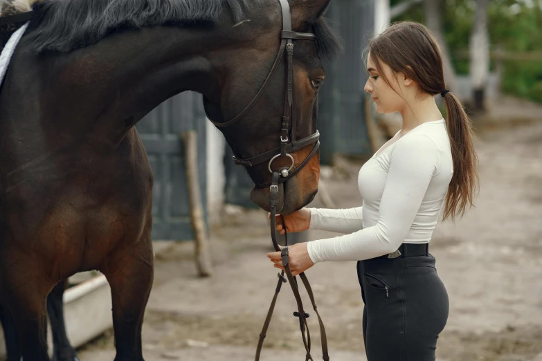 a woman holding the lead to a horse while it stands on a dirt road