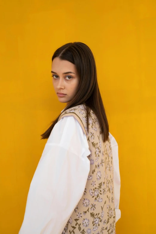 woman with long hair standing up against yellow wall