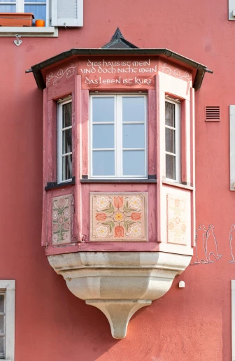 a red building with pink paint and two white windows