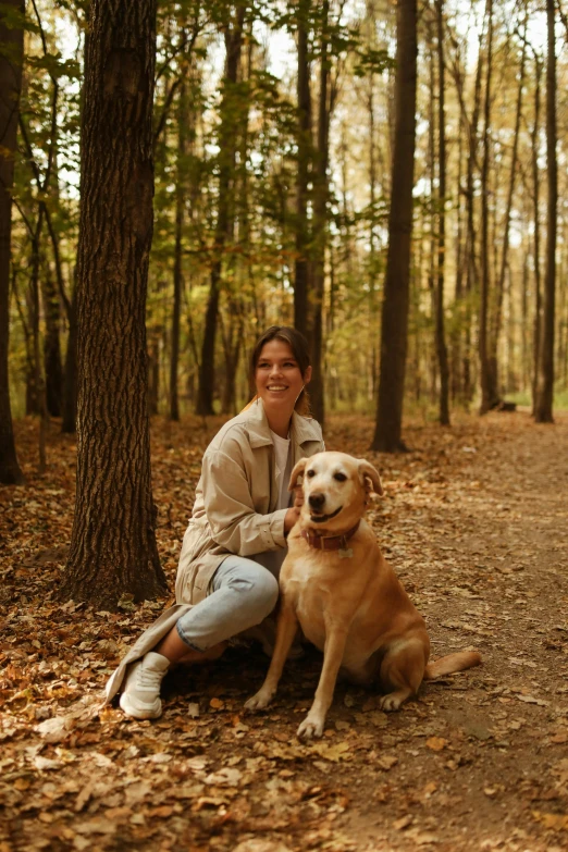 the girl is sitting next to her dog in the woods