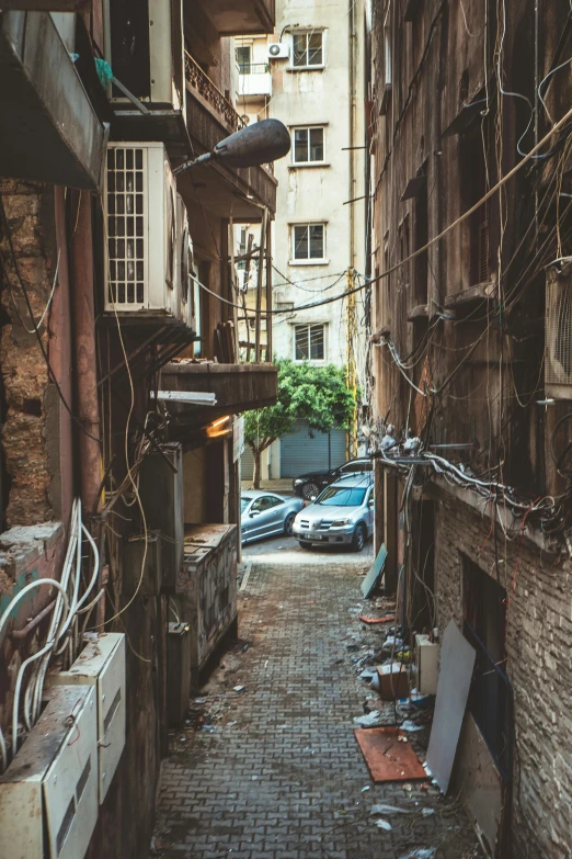 a narrow alley with electrical cables and a couple cars parked nearby