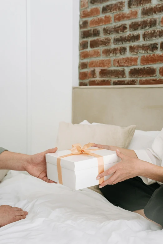 two people exchanging a present box on a bed