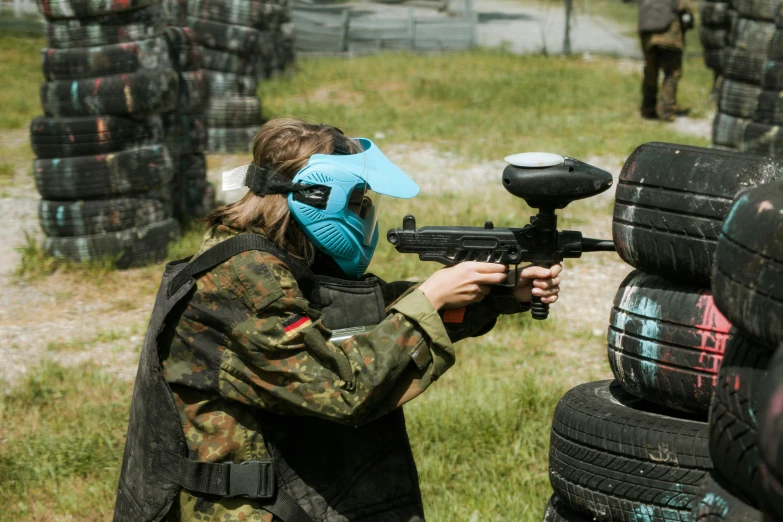 a woman with a mask is aiming at a paintball