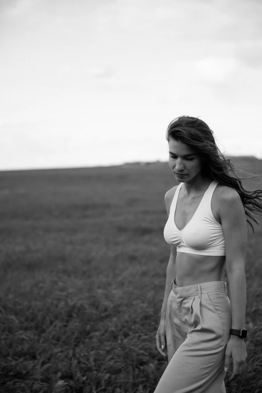 a woman walking across an open field next to a tall grass tree