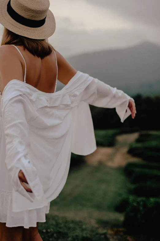 a girl in a hat and a white dress standing near a field