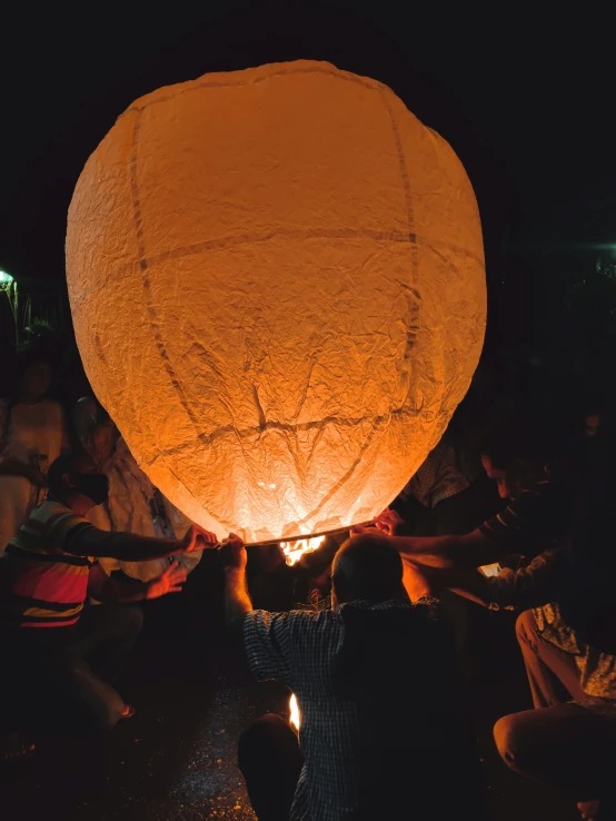 some people sitting down in the dark while a large paper ball is lifted