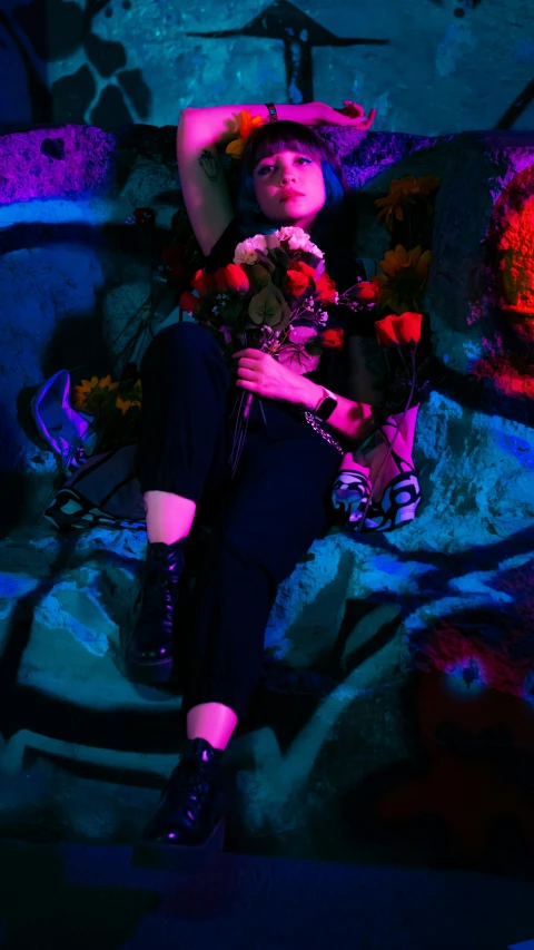 a woman sitting down next to flowers and a purple wall