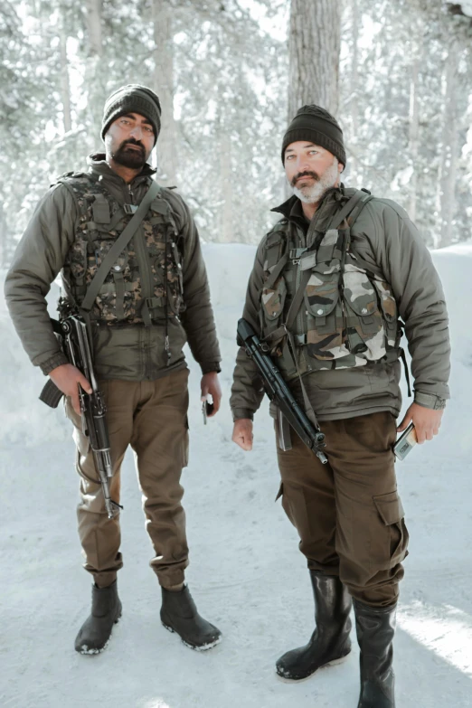 two men standing in the snow with rifles