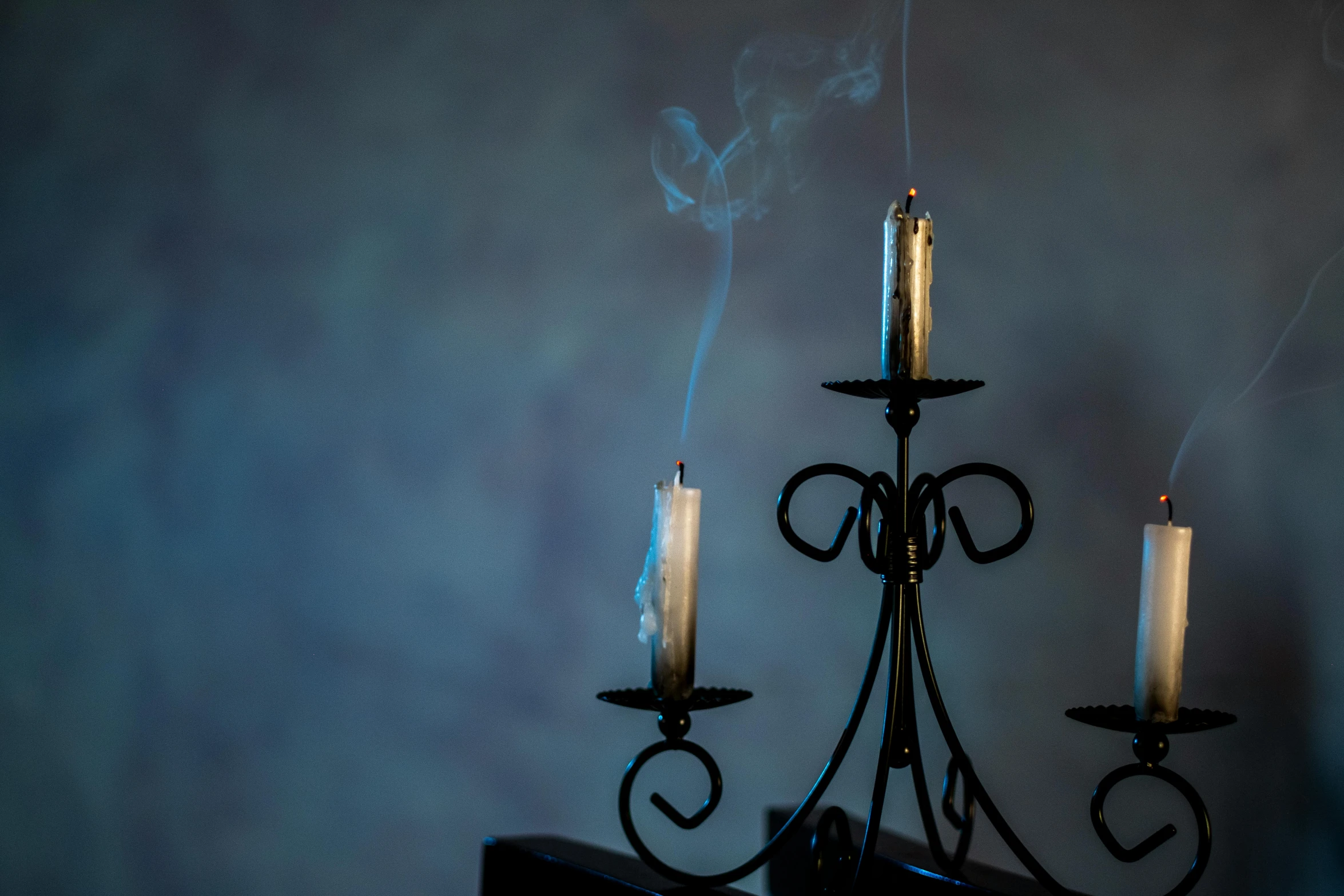 a wrought iron chandelier has three candles and a black light