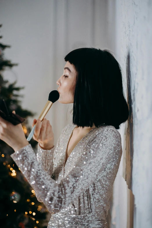 woman with brush on cheek near christmas tree