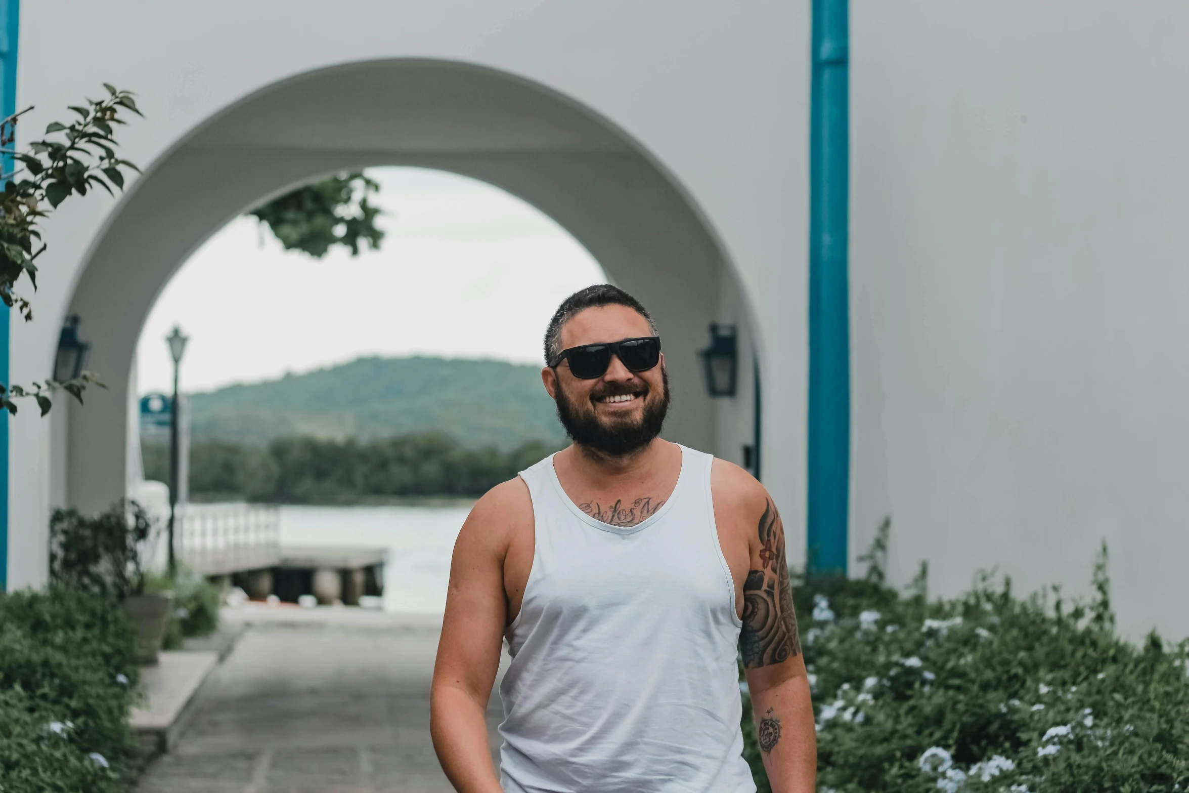 man in white tank top wearing sunglasses in front of an arch