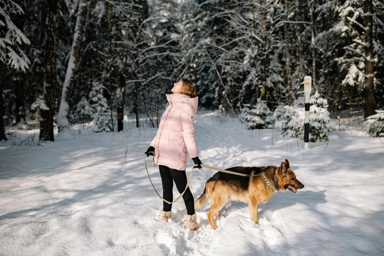 a woman in a pink coat and hat walking a dog