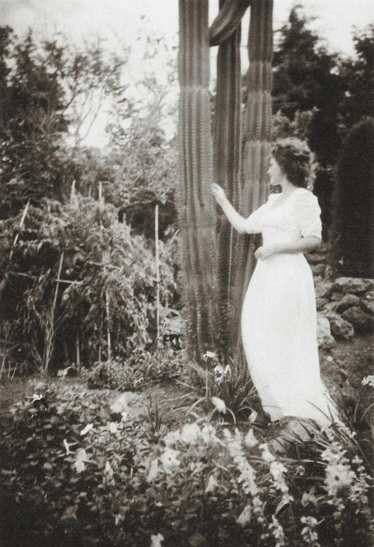 a woman in a dress is standing next to a tree