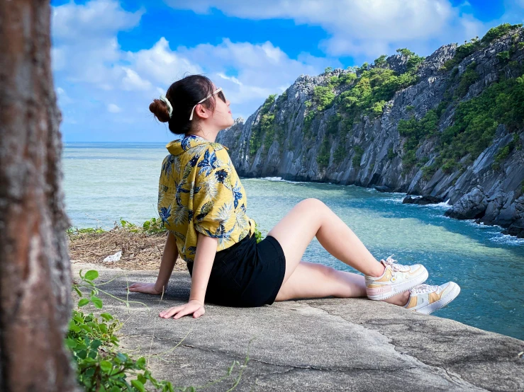 the woman is sitting on the cliff overlooking the water