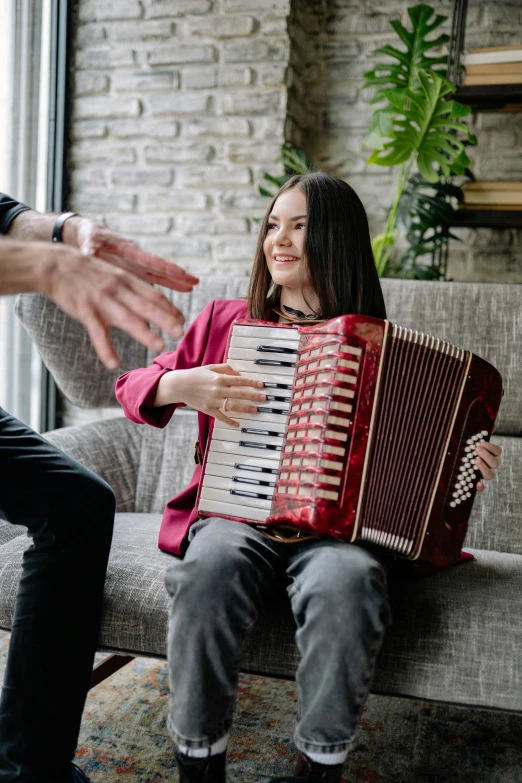 a woman smiles while playing an accordion with a man standing near