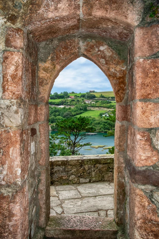 an old, round window frame that shows a lake in a field