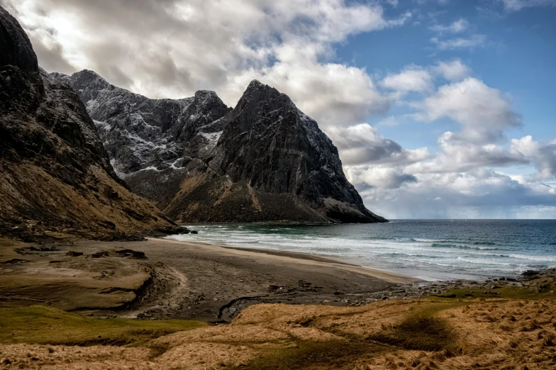 a beach surrounded by mountains on a cloudy day
