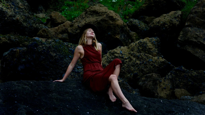 a woman sitting on rocks by herself wearing a red dress