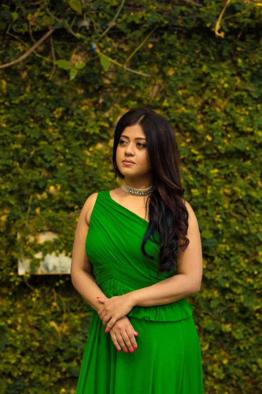 a woman wearing a green dress in front of a hedge
