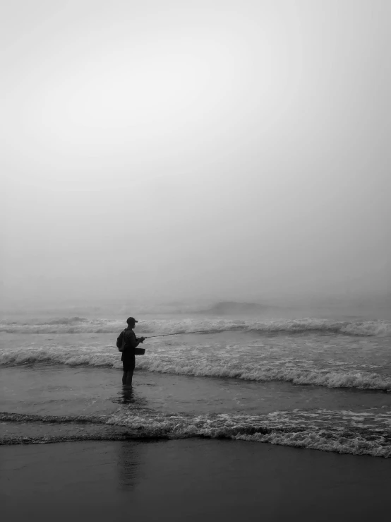 a man standing on the shore near an ocean holding a fish