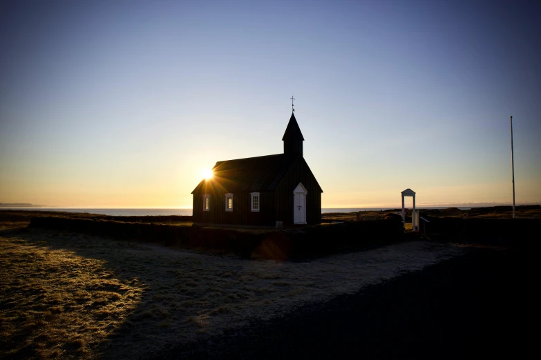 a small church building on a gravel road in front of a grassy area