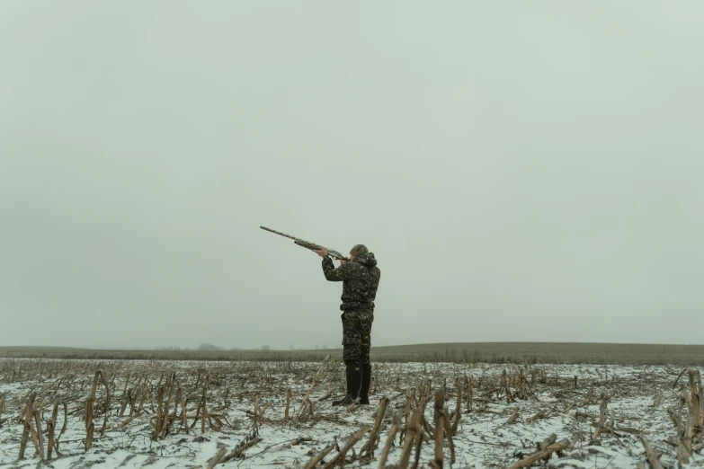 a man in winter gear holding a rifle in a snow covered field