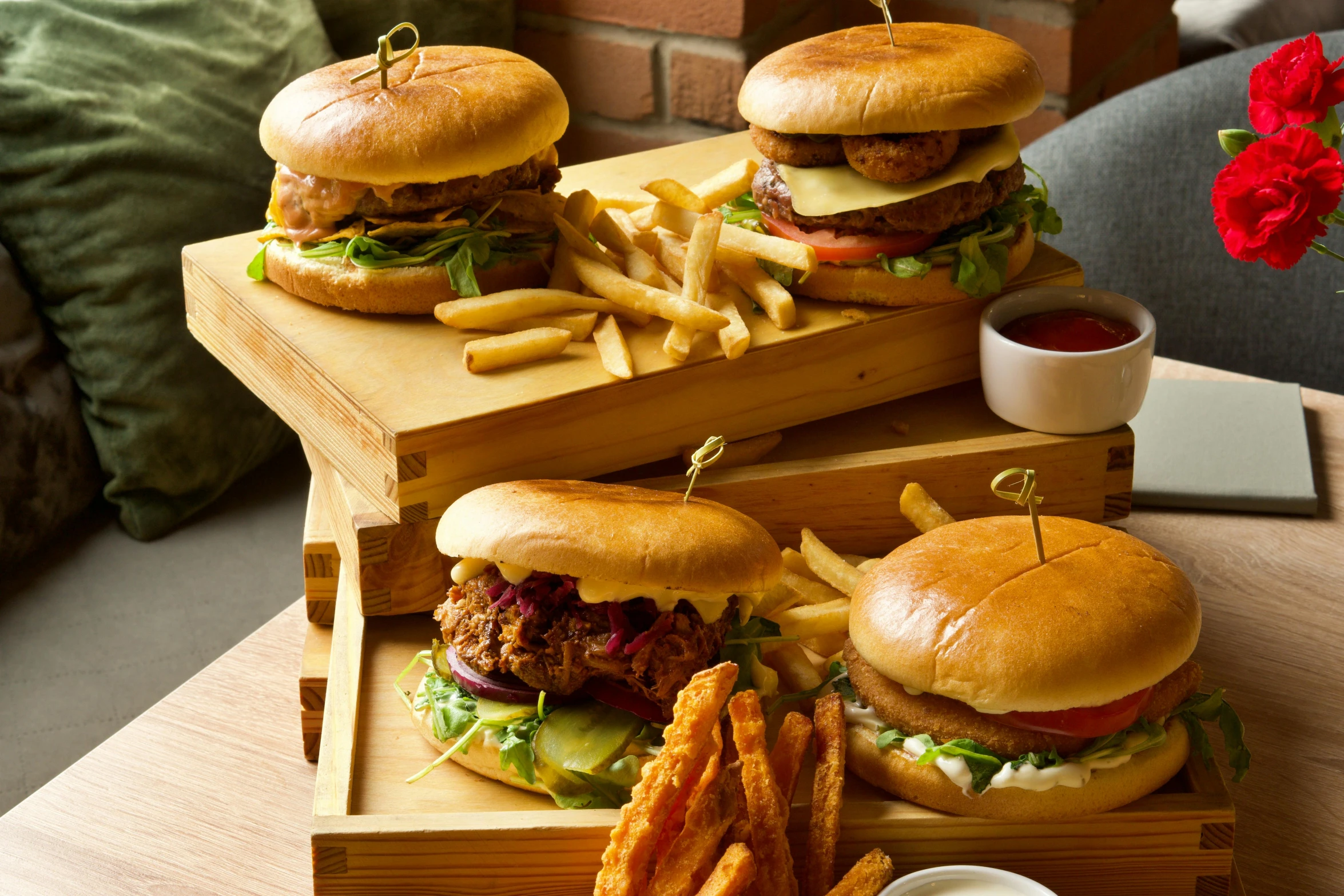 three burgers and fries in wooden boxes with a flower on a table