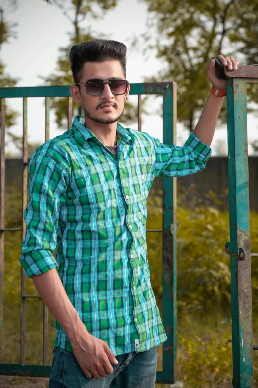 a young man wearing glasses and leaning on a gate