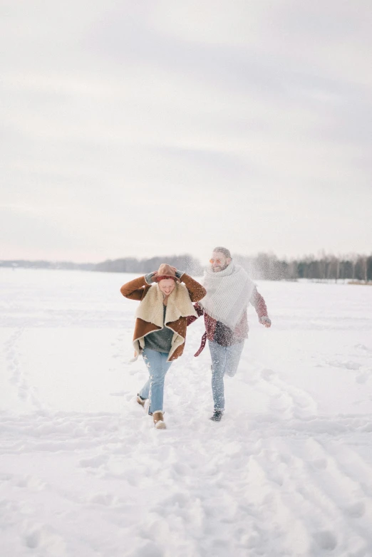 a man and woman walking through the snow in a field