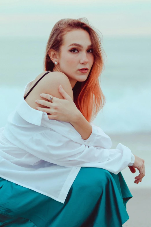 a girl with red hair sitting on a ledge by the ocean