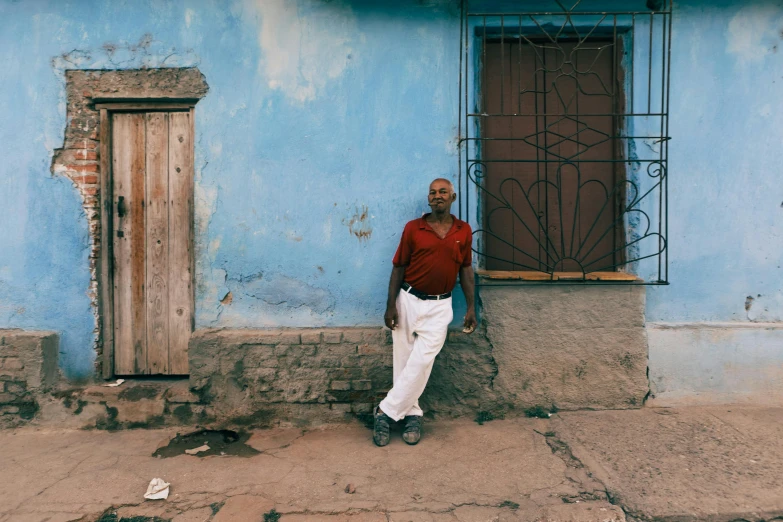 a man leans against a blue and gray building with an iron grilled door