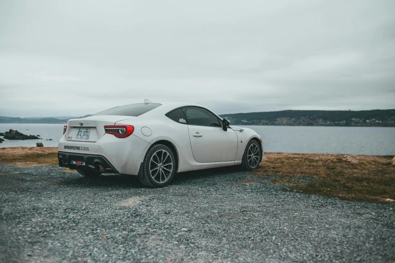 the toyota 86 coupe is parked next to a lake