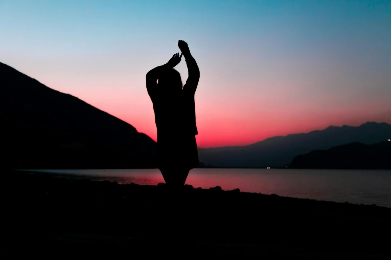 a man standing next to the water at dusk raising his arm up