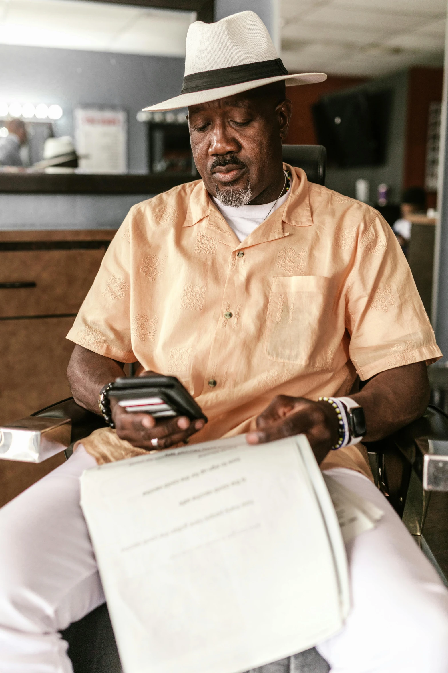 a man in a chair holding a piece of paper and looking at his cell phone