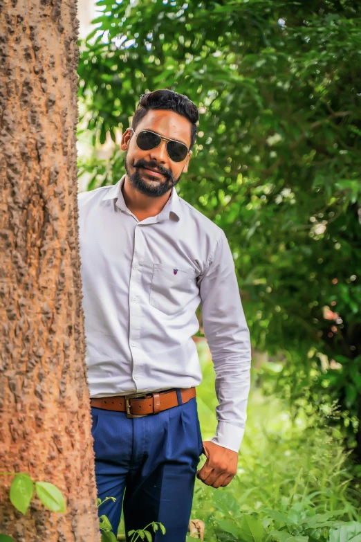 a man in sunglasses leans against a tree