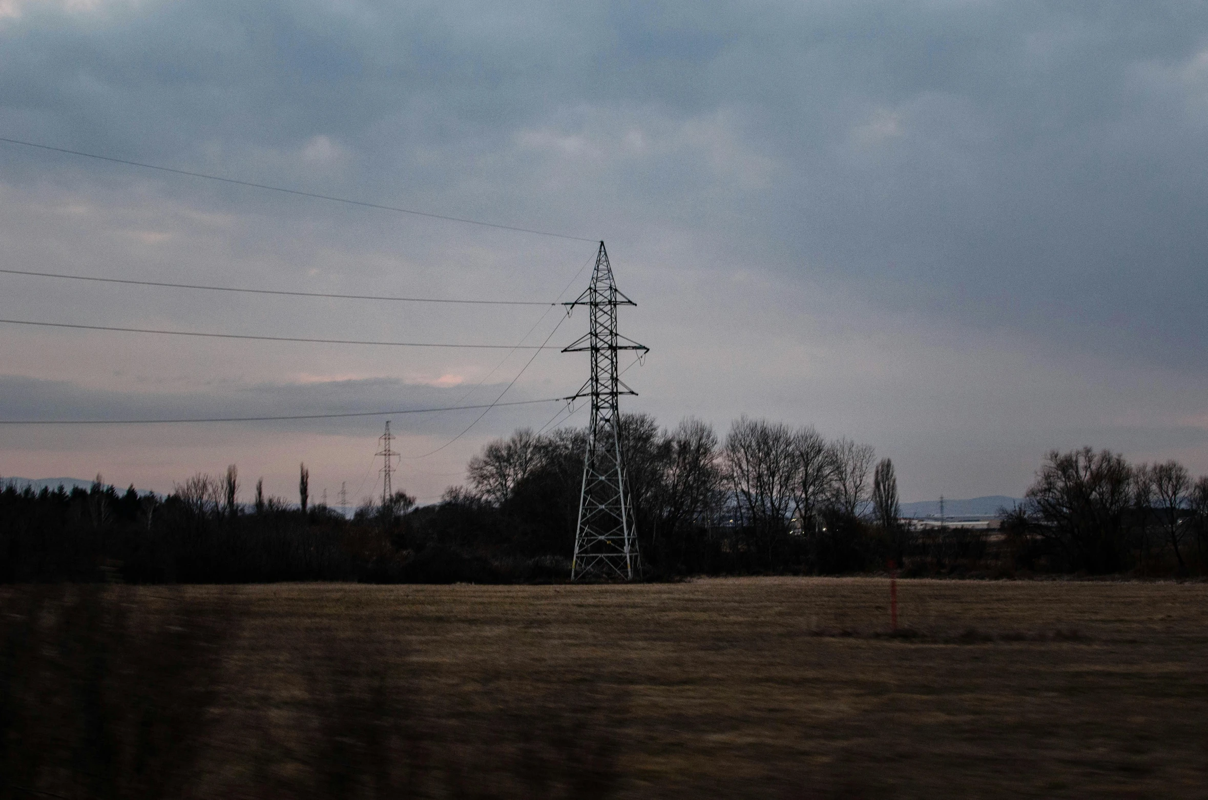 an electric pole near a grassy field and power lines