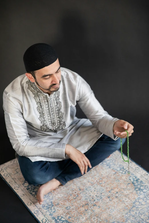 a man sitting on top of a rug tying soing green