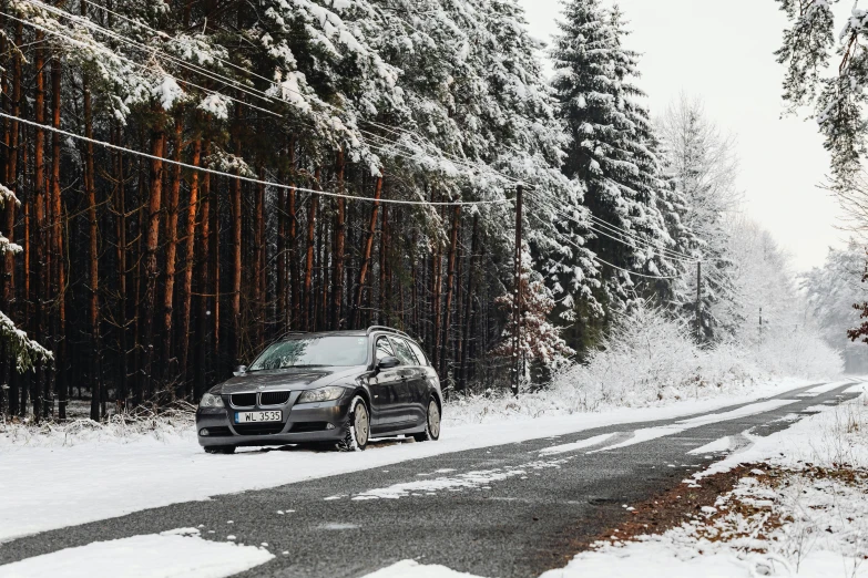 a car driving down a snowy road past pine trees